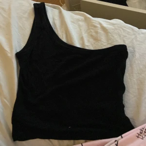 Svart oneshoulder topp XS - Säljer en svart oneshoulder topp från Shein i storlek XS. Toppen har en asymmetrisk design med en axel och är tillverkad i en mjuk blandning av viskos och polyester. Perfekt för dig som gillar stilrena och trendiga plagg.