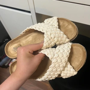 Tofflor  - Säljer ett par snygga beige sandaler med breda, flätade remmar. Perfekta för sommaren och riktigt sköna att gå i. Sulan är vit undertill och ovandelen har en mjuk känsla. Använda två gånger så nästintill nya:)
