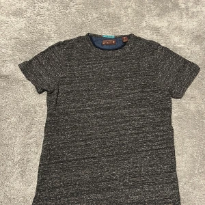 Mörkgrå t-shirt från Salon Bizarre - Säljer en mörkgråmelerad t-shirt från Salon Bizarre. T-shirten har rund halsringning och korta ärmar. Materialet är mjukt och bekvämt, perfekt för vardagsbruk. Enkel och stilren design utan tryck.