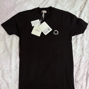 Svart t-shirt från Moncler - Säljer en svart t-shirt från Moncler med rund hals och liten broderad Moncler-logga på bröstet. T-shirten är i mjuk bomull och har en klassisk passform. Perfekt för dig som gillar stilrena plagg med exklusiv känsla. (Sitter som M)