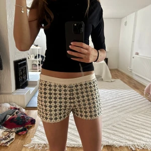 Mönstrade shorts med beige midja - Säljer ett par snygga shorts med svart och vitt rutmönster och beige midja. De har en normal passform och är perfekta för sommaren. Materialet känns mjukt och bekvämt, troligen bomull eller syntet.