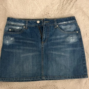 Jeanskjol från Vila - Säljer en klassisk blå jeanskjol från Vila med femficksmodell och snygga detaljer på bakfickorna. Kjolen har bälteshällor och stängs med dragkedja och knapp framtill. Perfekt till sneakers eller boots!