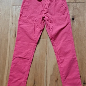 Rosa chinos med smal passform - Säljer ett par snygga rosa chinos med smal passform. Byxorna har klassisk design med fickor fram och bak samt medföljande extra knapp. Perfekta för dig som vill sticka ut med färg i vardagen.