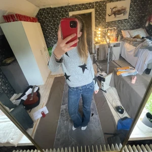 Grå stickad tröja med svarta stjärnor - Säljer en grå stickad tröja med stora svarta stjärnor. Tröjan har rund halsringning, långa ärmar och ribbade muddar vid ärmslut och nederkant. Perfekt för dig som gillar en cool och avslappnad stil.