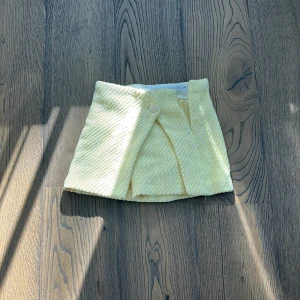 Gul omlottkjol från Zara - Söt gul omlottkjol från Zara i strukturvävt tyg. Kjolen har en knapp framtill och är designad med inbyggda shorts under för extra komfort. Perfekt för dig som gillar en fräsch och somrig look.