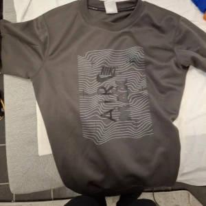 Grå Nike Air Max sweatshirt - Säljer en grå Nike Air Max sweatshirt med tryckt Nike-logga och vågigt mönster på bröstet. Tröjan har rund halsringning och långa ärmar med Air Max-detaljer längs ärmarna. Perfekt för en sportig och avslappnad stil. Kan prata om att sänka priset