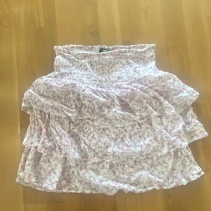 Blommig volangkjol från BikBok - Somrig volangkjol från BikBok i vitt med små rosa blommor. Kjolen har resår i midjan och flera lager volanger som ger en luftig känsla. Perfekt för varma sommardagar och funkar att matcha med en enkel topp.