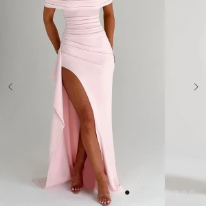 Ljusrosa offshoulder balklänning  med slits - Elegant ljusrosa långklänning med offshoulder-design och figurnära passform. Klänningen har en hög slits framtill och draperade detaljer över byst och midja. Perfekt för balen!!