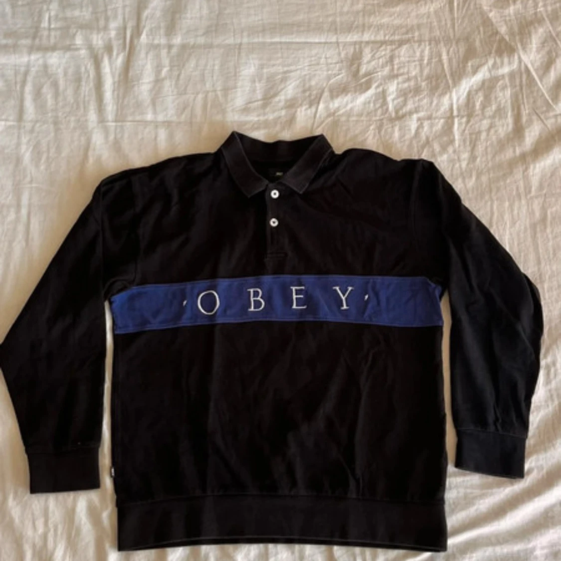 Svart pikétröja från OBEY med blå detalj