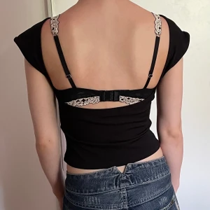 Svart öppen rygg topp från Cider - Säljer en svart topp med öppen rygg från Cider. Toppen har korta ärmar och en snygg öppen rygg med bredare axelparti. Perfekt för dig som gillar minimalistisk stil med en twist. Ej använd.
