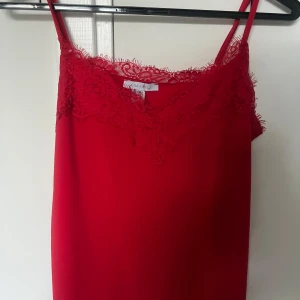 Röd spetslinnetopp från Amisu - Säljer en röd linnetopp från Amisu med tunna axelband och vacker spetsdetalj längs urringningen. Topp i mjukt material och feminin design. Säljer den då den kommer till väldigt liten användning, har då använt den 2 gånger och den är i storlek Xs.