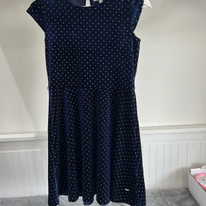 Mörkblå prickig klänning från Hampton Republic - Supersöt mörkblå klänning från Hampton Republic med små guldprickar. Klänningen har rund halsringning och är ärmlös, perfekt för speciella tillfällen. Mjuk och glansig yta som ger en lyxig känsla.