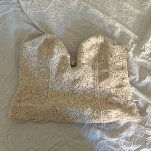 Beige tubtopp från H&M Edition - Säljer en beige tubtopp från H&M Edition. Toppen har en strukturerad yta och är axelbandslös med smock baktill för extra komfort. Perfekt att styla till sommarens outfits!