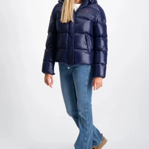 Mörkblå dunjacka från Ralph Lauren - Säljer en mörkblå, glansig dunjacka från Ralph Lauren med huva och dragkedja framtill. Jackan har två stora fickor och en liten röd logga på bröstet. Perfekt för kyliga dagar och riktigt snygg till jeans.