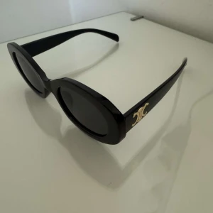 Svarta ovala solglasögon Celine - Stilrena svarta solglasögon med oval form köpta på den gula appen. Bågarna är i svart plast och har ikoniska C guldfärgade loggor på sidorna.🌺 