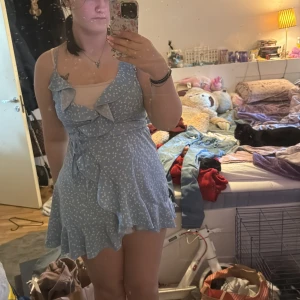 Ljusblå omlottklänning med hjärtmönster från SHEIN - Supersöt ljusblå kortklänning från SHEIN med vitt hjärtmönster. Klänningen har volangdetaljer, omlottmodell och smala axelband. Perfekt för sommarens alla tillfällen! Materialet är lätt och luftigt.