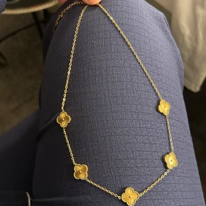 Guldigt halsband med blommiga detaljer - Säljer ett elegant halsband i guldton med fem blommiga, fyrkantiga hängen. Kedjan är tunn och smidig, perfekt för att ge en stilren touch till din outfit. Passar dig som gillar unika och feminina smycken. Materialet är rostfritt och kan användas när man även badar.