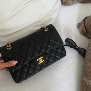  axelväska  - Säljer en klassisk svart quiltad axelväska med guldfärgade kedjedetaljer. Insidan är vinröd  