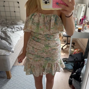 Blommig axelbandslös kortklänning - Säljer en söt axelbandslös kortklänning med volangkant och blommigt broderat mönster i pastellfärger. Storlek S från Loavies💗