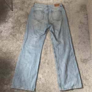 Ljusblå jeansbyxor från NA-KD - Ljusblå jeansbyxor från NA-KD med raka ben och klassiska bakfickor. Byxorna har normal passform och är tillverkade i denim med en snygg vintagekänsla. Perfekta för en avslappnad stil.