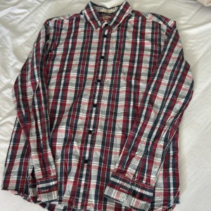 Rutig skjorta från Levi's - Säljer en klassisk rutig skjorta från Levi's i rött, blått och vitt. Skjortan har långa ärmar, knappar framtill och en normal passform. Perfekt för dig som gillar en tidlös stil med lite färg.