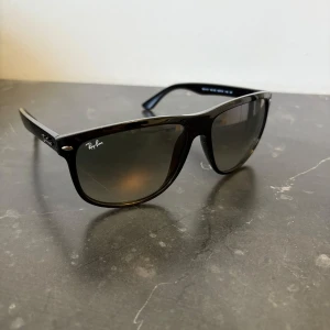 Ray-Ban boyfriend - Klassiska svarta solglasögon från Ray-Ban med Wayfarer-inspirerad form. Bågarna är i blank svart plast och glasen är mörka. Perfekt accessoar för en stilren look.