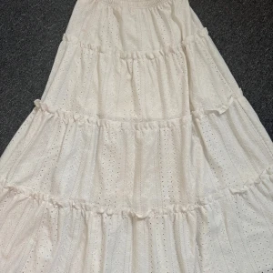 Vit långkjol med volanger från Shein - Säljer en romantisk vit långkjol från Shein med broderade detaljer och flera volanger. Kjolen har resår i midjan och är tillverkad i ett lätt bomullsmaterial. Perfekt för varma dagar och en bohemisk look. Den är lite missfärgad vid midjekanten, men syns ej i alla ljus och på långt håll🙏🏼