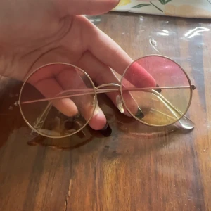 Runda solglasögon med rosa och gula glas - Coola runda solglasögon med tunna guldfärgade metallbågar och färgade glas i rosa och gult. Perfekta för att sticka ut och ge en retrovibe till din outfit.