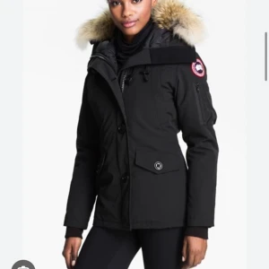 Svart vinterjacka med pälskrage från Canada Goose - Säljer en svart vinterjacka från Canada Goose med pälskantad huva och klassisk logga på ärmen. Jackan har dragkedja och knappar framtill samt fickor med lock. Perfekt för kalla dagar.  be om en bild!💞