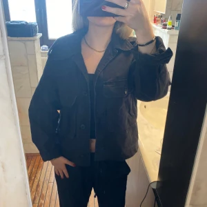 Svart jacka med stora fickor - Säljer en svart overshirt med stora bröstfickor och knäppning framtill. Jackan har en avslappnad passform och klassisk krage. Perfekt att slänga över en t-shirt eller hoodie för en cool look.