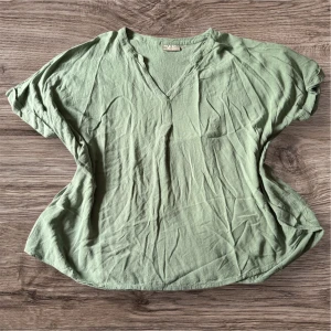 Ljusgrön blus från Only Carmakoma - Säljer en ljusgrön blus från Only Carmakoma. Blusen har korta ärmar, v-ringning och är tillverkad i ett lätt, strukturerat tyg. Perfekt för varmare dagar och enkel att matcha med olika outfits.