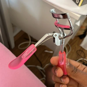 Rosa ögonfransböjare i metall och plast - En ögonfransböjare med handtag i genomskinlig rosa plast och metallram. Silikonplattan är också rosa, vilket ger ett färgglatt intryck. Perfekt för att lyfta och böja fransarna snabbt och enkelt.