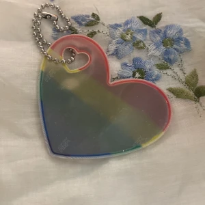 Reflex i hjärtform med regnbågsfärger - Säljer en söt reflex i form av ett hjärta med regnbågsfärgad kant och en liten hjärtformad öppning för kedjan. Perfekt att hänga på väskan eller jackan för extra synlighet.