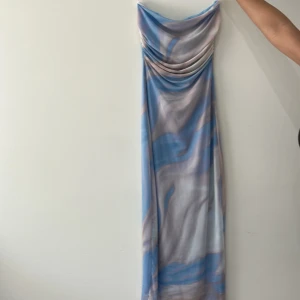 Blå och lila långklänning med draperad urringning - Säljer en långklänning med vackert mönster i blått, lila och beige. Klänningen har en draperad, v-ringad urringning och är ärmlös. Perfekt för sommarens tillfällen!