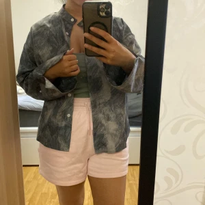 Grå mönstrad skjorta med knappar - Säljer en grå skjorta med abstrakt mönster och knappar framtill. Skjortan har lång ärm och rak passform med klassisk krage. Perfekt att styla öppen över ett linne eller stängd som den är.