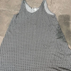 Svartvit mönstrad ärmlös klänning - Säljer en svartvit ärmlös klänning med små geometriska mönster. Klänningen har en avslappnad passform och är perfekt för varma dagar. Tunn och lätt i materialet, enkel att styla med sneakers eller sandaler.