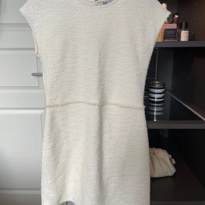 Vit kortklänning i bouclé - Säljer en söt vit kortklänning i bouclé-liknande material. Klänningen har rund halsringning, korta ärmar och en rak passform som ger en stilren look. Perfekt för sommarens tillfällen, konfermation eller studentfirande. Endast använd en gång💕