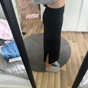 Svart långkjol med slits - Säljer en svart långkjol med slits på sidan. Kjolen har en tight passform och är enkel i modellen, perfekt att styla med en stickad tröja eller crop top. Materialet känns mjukt och följsamt. säljer på grund av att den är lite för kort för mig