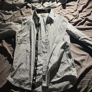 Randig skjorta från Zara Man - Snygg skjorta från Zara Man med smala svarta och vita ränder. Klassisk krage, svarta detaljer på insidan av kragen och knappslån samt vita knappar. Långärmad och i mjuk bomull, perfekt för en clean och stilren look.