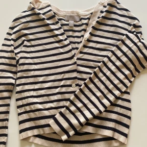 Randig kofta från H&M i XS - Beige och svart randig kofta från H&M i storlek XS. Koftan har v-ringning, knappar framtill och långa ärmar. Tillverkad i mjukt, stickat material som är skönt mot huden.