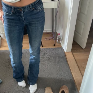 blå raka jeans med bootcut - Säljer ett par klassiska blå jeans med raka ben och lätt bootcut. Jeansen har fem fickor, normalhög midja och är tillverkade i robust denim. Snygg tvätt med lite slitningar för en avslappnad look. Perfekta till sneakers eller boots. ‼️byxorna har en liten vit fläck som man borde kunna få bort, vet inte vad där är för något‼️