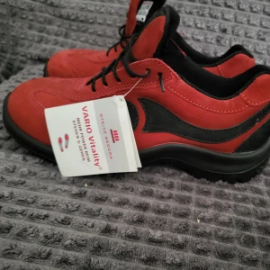 Röda skyddskor från Steitz Secura - Snygga röda skyddskor från Steitz Secura med svarta detaljer och svart sula. Skorna har snörning och är tillverkade i mocka med inslag av syntet. Perfekta för dig som vill ha en sportig och bekväm stil med lite edge.