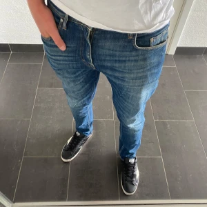 Blå jeans från Tiger of Sweden - Säljer ett par klassiska blå jeans från Tiger of Sweden. Jeansen har en rak passform, snygga slitningar och kontrastsömmar. Tillverkade i bomull och har fem fickor samt gylf med dragkedja. Perfekta för en stilren och avslappnad look.