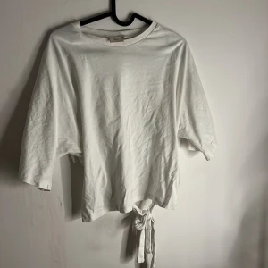 Vit knyttröja från Nelly - Vit tröja från Nelly med avslappnad passform och knytning där bak. Modellen har vida, trekvartsärmar och rund halsringning. Perfekt för en chill och stilren look. Tillverkad i mjuk bomull som känns skön mot huden. är jättebra skick och har använts ca tre gånger💕