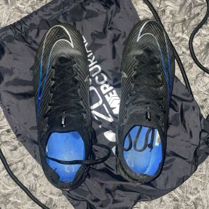 Nike Mercurial Zoom fotbollsskor svart/blå - Säljer ett par Nike Mercurial Zoom fotbollsskor i svart med blå detaljer och vita swoosh-loggor. Diksutetara priset 