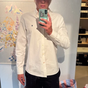 Vit skjorta från Morris Stockholm - Klassisk vit skjorta från Morris Stockholm med broderad logga på bröstet. Skjortan är i strl M och även i väldigt fint skick, endast använd ett fåtal gånger!