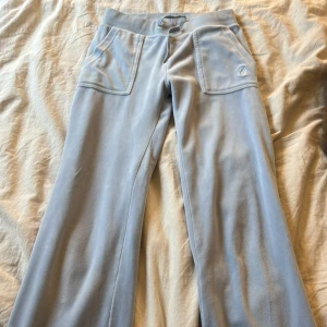 Ljusblå velourbyxor Juicy Couture XXS - Supermjuka ljusblå velourbyxor från Juicy Couture med bred resår i midjan, stora fickor fram och bak med silvriga detaljer. Tyvärr så har ”knapparna” till snörena lossnat, men inget som förstör byxan i sig. 💗