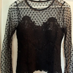 Svart spetsblus Ida Sjöstedt strl 36 - Supersnygg svart blus från Ida Sjöstedt med transparent mesh. Blusen har lång ärm och vackra spetsdetaljer framtill och nedtill. Storlek 36/ small. Köpare står för frakten.