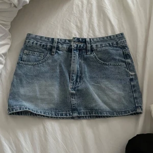 Blå jeanskjol med fickor - Säljer en klassisk blå jeanskjol i kort modell med fem fickor och bälteshällor. Kjolen har en snygg tvättad look och stängs med dragkedja och knapp framtill. Perfekt att styla med sneakers eller boots för en cool vibe. Aldrig använd , pris kan diskuteras vid snabb affär 🩷🥂
