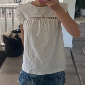 Vit blus med spets och volangärm💕 - Supersöt vit blus med broderade detaljer och små hålmönster. Blusen har volangärmar och en fin spetskant med blommor över bröstet. Perfekt till jeans eller kjol för en fräsch look. Materialet känns lätt och luftigt💕💕
